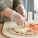 A person wearing Noble Products small powdered vinyl gloves putting cheese on a pizza.