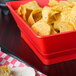 A red square serving basket filled with tortilla chips.