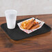 A Carlisle black fiberglass tray with a hot dog and french fries on it and a white plastic cup with a lid.