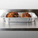 A stainless steel counter with two Durable Packaging foil roast pans filled with food.