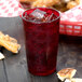 A Cambro ruby red plastic tumbler filled with red liquid and ice on a table with a basket of pretzels.