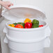 A person using a white Rubbermaid BRUTE container to store yellow peppers.