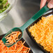 A person holding a Thunder Group green polycarbonate salad bar spoon over a bowl of shredded cheese.