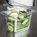 A clear plastic food pan with cucumbers and cheese on a counter.