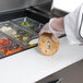 A person in gloves using a Traulsen sandwich prep table to cut a bagel.