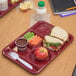 A Carlisle dark cranberry 6 compartment tray with a sandwich, carrots, and apples.