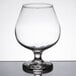 A Libbey brandy glass with a clear liquid inside on a table.