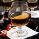 A Libbey brandy glass filled with brown liquid on a table.