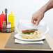 A hand reaching for a sandwich on a plate with a Cambro clear plate cover.
