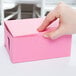 A person's hand opening a pink bakery box.