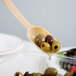 A beige Cambro salad bar spoon with olives on it.