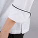 A close up of a Chef Revival white long sleeve coat with black piping on the sleeve.