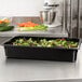 A black Cambro plastic food pan filled with green salad on a counter.