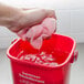 A hand holding a pink towel over a red bucket of water.