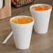 Two Dart white foam cups filled with orange liquid on a counter.