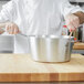 A chef stirring a Vollrath Wear-Ever sauce pan on a wooden surface.