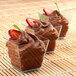 A row of Fineline green plastic cube bowls filled with chocolate mousse with strawberries on top.
