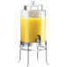 A Cal-Mil glass beverage dispenser with an ice chamber on a stand filled with orange juice.