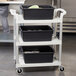 A speckled gray Cambro utility cart with three black shelves on it.