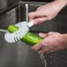 A person washing a cucumber with a Carlisle Sparta Spectrum vegetable brush.