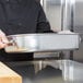 A chef holding a Vollrath aluminum roasting pan with handles.