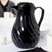 A black Vollrath SwirlServe coffee pitcher on a white table.