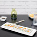 A rectangular white Tuxton china platter with a sushi roll on it.