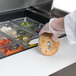 A person putting a bagel into a food container on a Traulsen sandwich prep table.