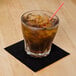 A glass with ice and a straw filled with brown liquid on a table with a Hoffmaster black beverage napkin.
