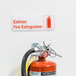 A red and white Tablecraft fire extinguisher sign on a wall above a fire extinguisher.