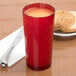 A red Cambro plastic tumbler on a white background next to a plate of bagel and a knife.