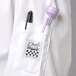 A close-up of the pocket of a white Chef Revival chef jacket with a purple pen in the pocket.