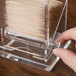 A person placing toothpicks in a clear plastic Cal-Mil toothpick dispenser.