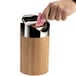 A hand putting a piece of paper into a Cal-Mil bamboo round counter trash bin.