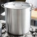 A Vollrath stainless steel pot cover on a large pot on a stove.