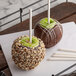 A green apple covered in chocolate and nuts on a Paper Pointed Candy Apple Stick.