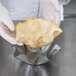 A person in gloves using a tortilla to shape a bowl over a metal bowl.