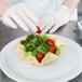 A gloved hand adds a cherry tomato to a salad in a Chicago Metallic tortilla bowl.