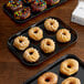 A black Cambro market tray holding donuts on a table in a bakery display.