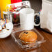 A muffin in a Durable Packaging clear plastic container with a hinged lid next to a cup of coffee.