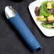 A navy blue Hoffmaster linen-like napkin with a silver spoon and a fork on a plate of salad.