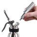 A hand using a Chef Master N2O cartridge to a metal whipped cream dispenser.
