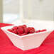 An Arcoroc flared bowl filled with raspberries on a red table.