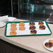 A Carlisle forest green Glasteel bakery tray holding chocolate covered doughnuts on a counter.