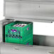A Traulsen school milk cooler with green milk crates inside.
