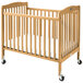 A natural wood L.A. Baby mini crib with wheels.