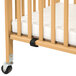 A L.A. Baby natural wood mini crib with wheels and a mattress.
