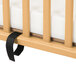 A L.A. Baby natural wood mini crib with a black strap on the mattress.