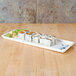 A Blue Bamboo melamine sandwich tray with a sushi roll on it on a wood table.