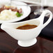 An American Metalcraft white porcelain gravy boat filled with brown sauce on a table.